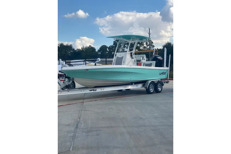 Slide: The Image of 2026 Mako 24 APEX boat on trailer, parked outdoors under a partly cloudy sky. - 1