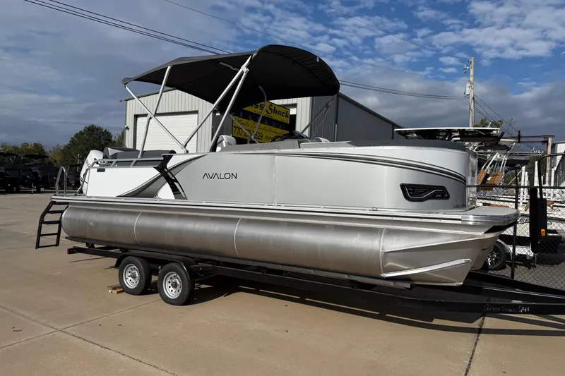 Slide: The Image of 2026 Avalon LSZ Quad Lounger Shift pontoon boat on trailer, parked outdoors. - 0
