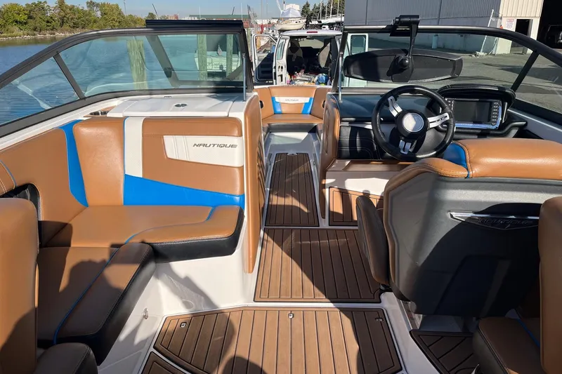 Slide: The Image of 2016 Nautique Super Air Nautique 230 interior with brown and blue seating, wooden flooring. - 7