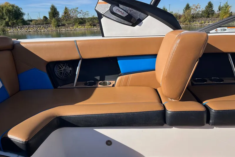 Slide: The Image of 2016 Nautique Super Air Nautique 230 interior with tan and blue seating, cup holders, and speaker. - 9