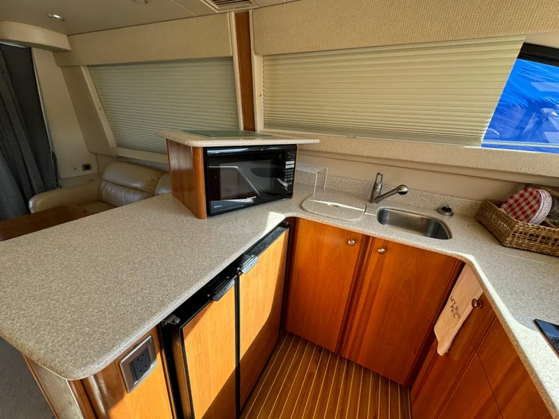 Slide: The Image of 2004 Meridian 381 Sedan yacht interior with kitchenette, featuring microwave, sink, and wooden cabinetry. - 21