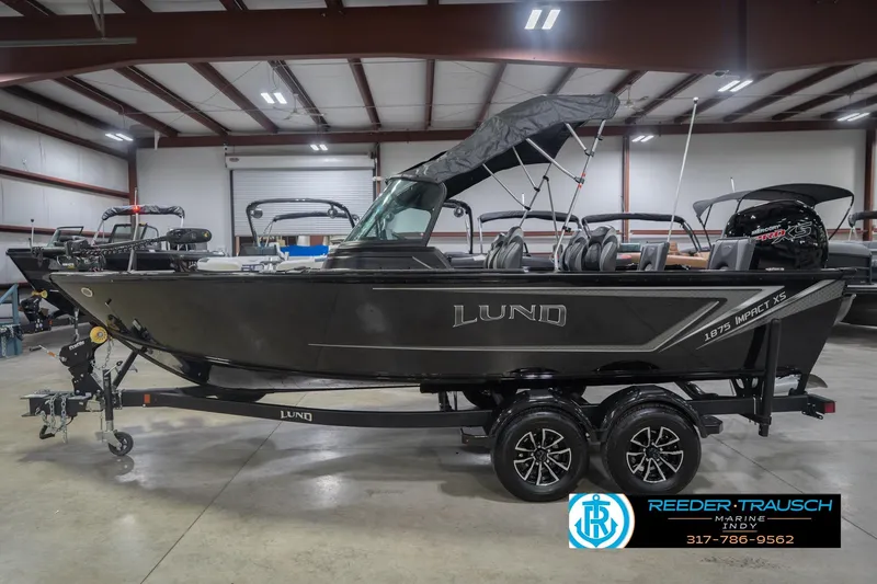 Slide: The Image of 2026 Lund 1875 Impact XS boat in showroom, featuring sleek design and dual-axle trailer. - 11