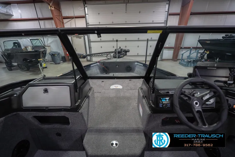 Slide: The Image of 2026 Lund 1875 Impact XS boat interior in a showroom with steering wheel and control panel. - 17
