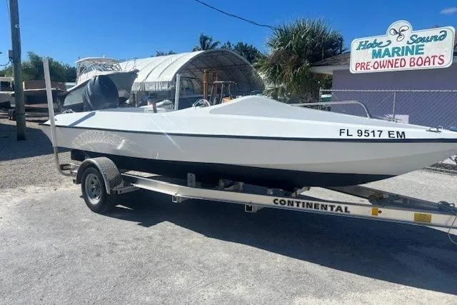 Slide: The Image of White JJM VS 1985 boat on trailer at marine dealership, sunny day. - 2