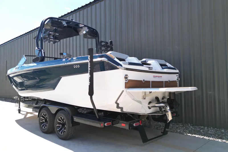 Slide: The Image of 2026 Nautique Super Air Nautique GS24 boat on trailer, parked beside a metal building. - 22