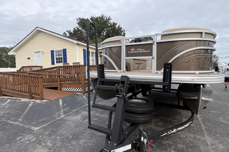 Slide: The Image of 2024 Sun Tracker SportFish 22 DLX pontoon boat on trailer near a yellow house. - 5