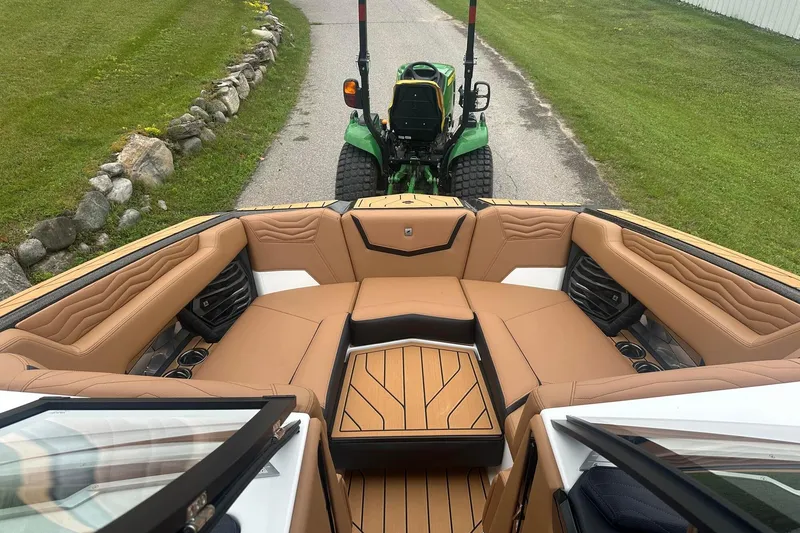 Slide: The Image of 2025 Nautique Super Air Nautique G23 boat interior with tan seating, parked on a grassy path. - 37