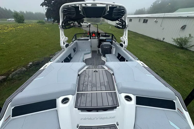 Slide: The Image of 2025 Nautique Super Air Nautique GS22 boat interior with seating and deck, parked on grass. - 11