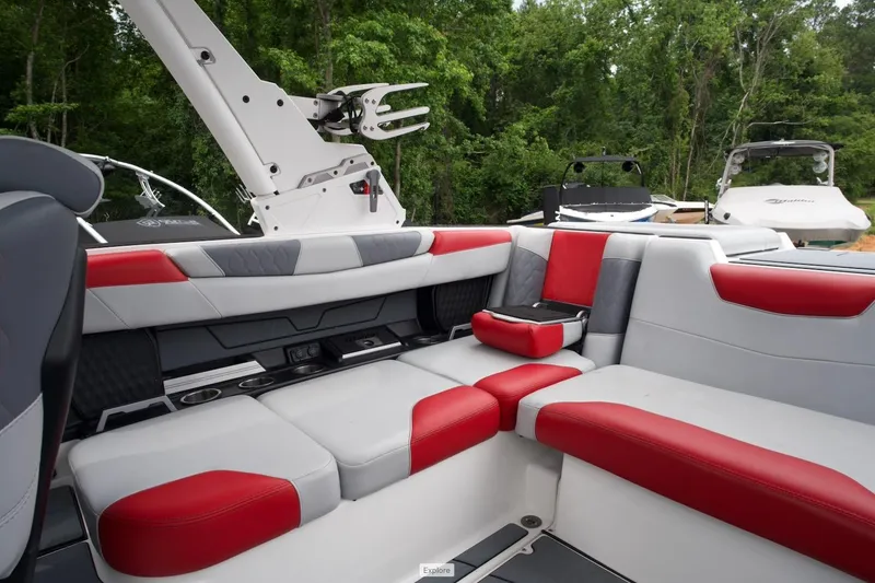 Slide: The Image of Interior of 2021 Malibu M220 boat with red and gray seating, surrounded by lush greenery. - 7