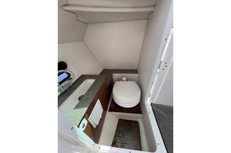 Slide: The Image of 2020 Four Winns HD240 OB boat interior with compact bathroom, featuring a toilet and sink. - 14