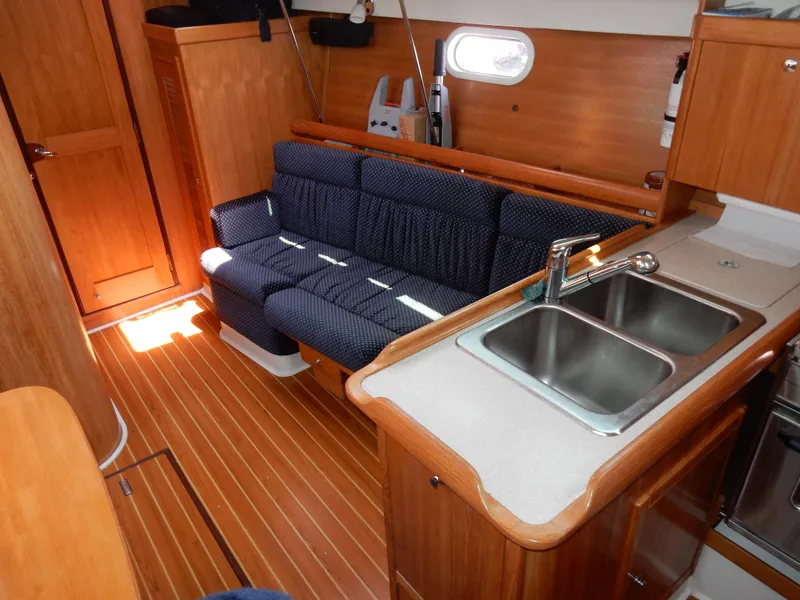 Slide: The Image of 2004 Catalina 350 yacht interior with wooden flooring, blue sofa, and kitchen sink. - 22
