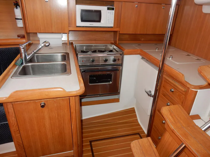 Slide: The Image of 2004 Catalina 350 yacht kitchen with wood cabinetry, dual sink, stove, and microwave. - 23