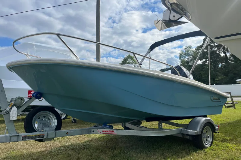 Slide: The Image of 2026 Boston Whaler 130 Super Sport boat on trailer, parked outdoors under cloudy sky. - 16