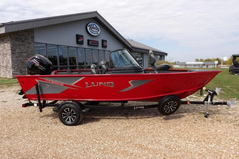 The Image of 2026 Lund 1775 Adventure Sport boat in red, parked outside a marine center. - 2