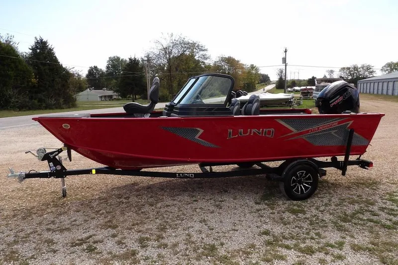 Slide: The Image of 2026 Lund 1775 Adventure Sport boat in red, parked on a gravel driveway. - 8