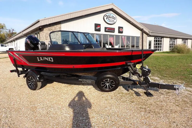 The Image of 2026 Lund 1775 Impact XS Sport boat in front of marine center, red and black design. - 0