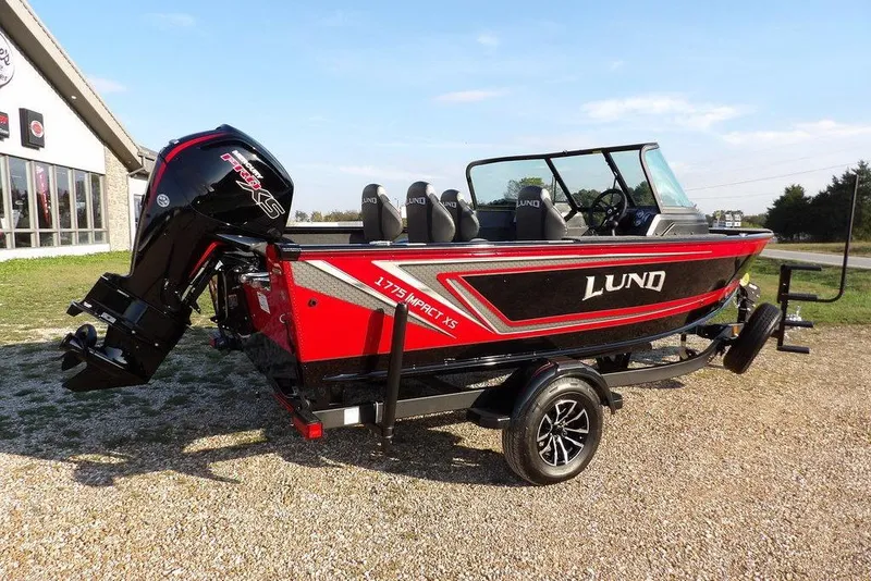 Slide: The Image of 2026 Lund 1775 Impact XS Sport boat on trailer, red and black design, parked outdoors. - 17