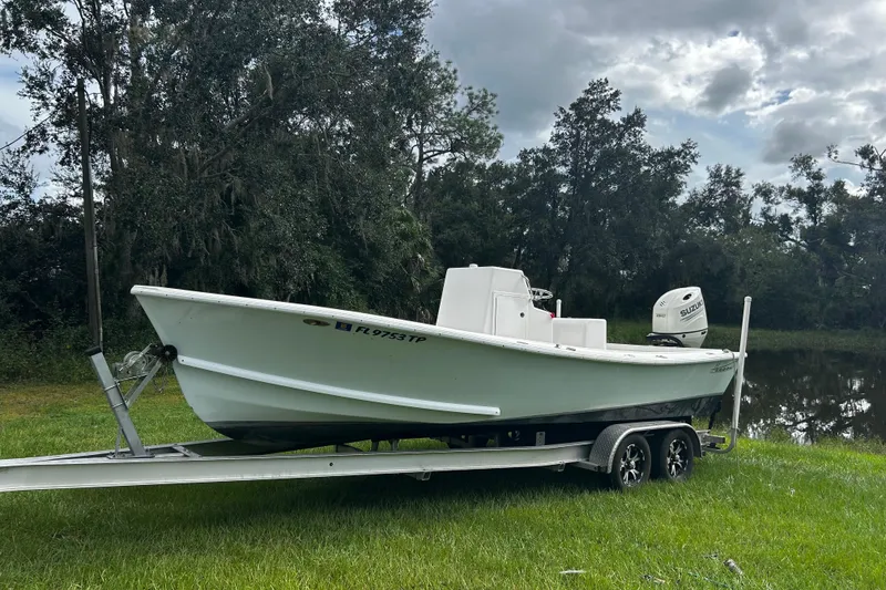Slide: The Image of 2024 Hanson 23 boat on trailer, parked on grass near a pond, under cloudy sky. - 0