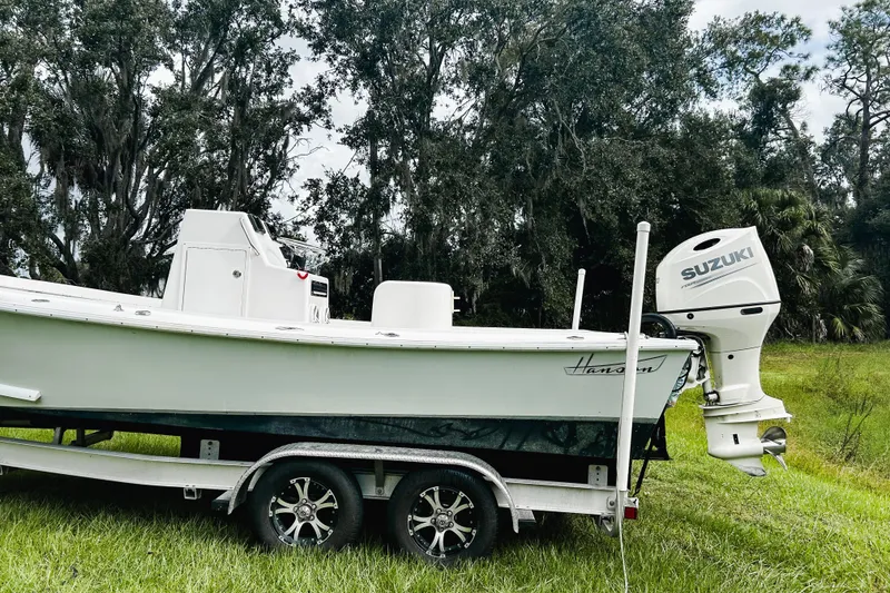 Slide: The Image of 2024 Hanson 23 boat on trailer with Suzuki outboard, set against a lush green backdrop. - 1