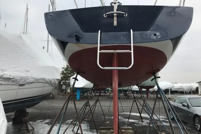 Slide: The Image of 1997 JBoat J 105 sailboat on stands in a boatyard, overcast sky. - 24