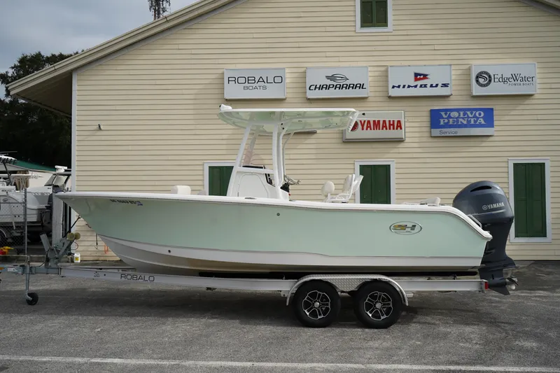 The Image of 2022 Sea Hunt Ultra 229 boat on trailer, parked outside dealership with various brand signs. - 0