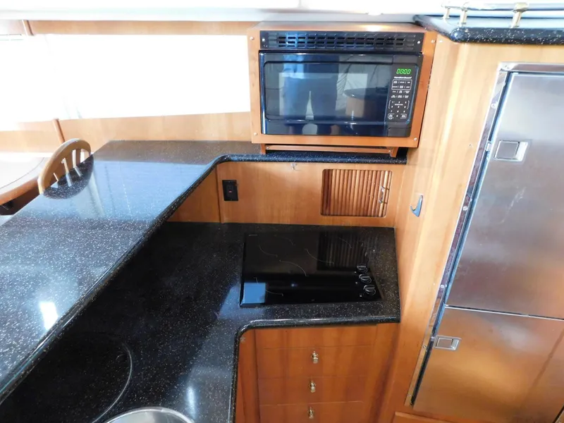 Slide: The Image of 2003 Carver 444 Cockpit Motor Yacht kitchen with microwave, stovetop, and sleek countertops. - 27