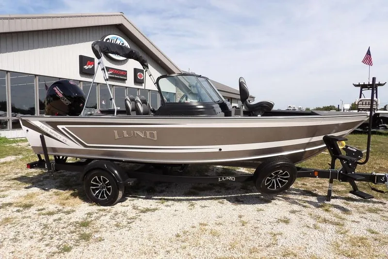 The Image of 2026 Lund 1875 Impact XS Sport boat on trailer, parked outside dealership. - 1