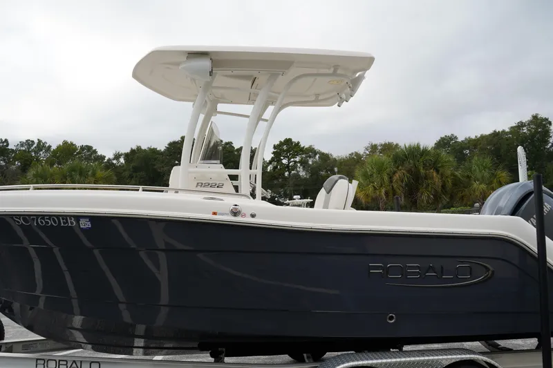 Slide: The Image of 2023 Robalo R222 Explorer boat on trailer, side view with trees in background. - 6