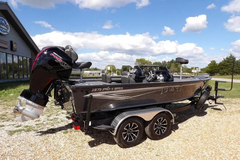 Slide: The Image of 2026 Lund 1875 Pro-V Bass XS boat on trailer, parked outdoors under a blue sky. - 12