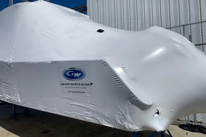 Slide: The Image of 2026 Grady-White Canyon 306 boat covered in protective wrap near a metal building. - 1
