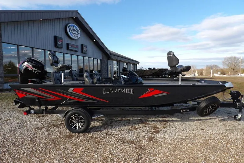 Slide: The Image of 2026 Lund 1875 Renegade boat with red accents parked outside a marine center. - 3