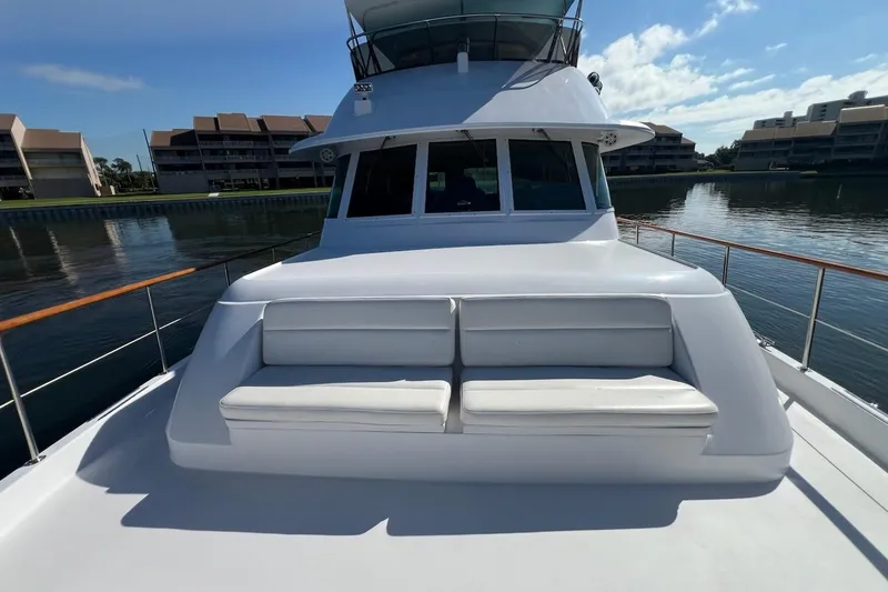 Slide: The Image of 1985 Hatteras 58 Motor Yacht with white seating on deck, docked near waterfront buildings. - 12