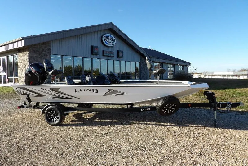 The Image of 2026 Lund 1975 Renegade boat on trailer outside dealership, clear blue sky. - 2