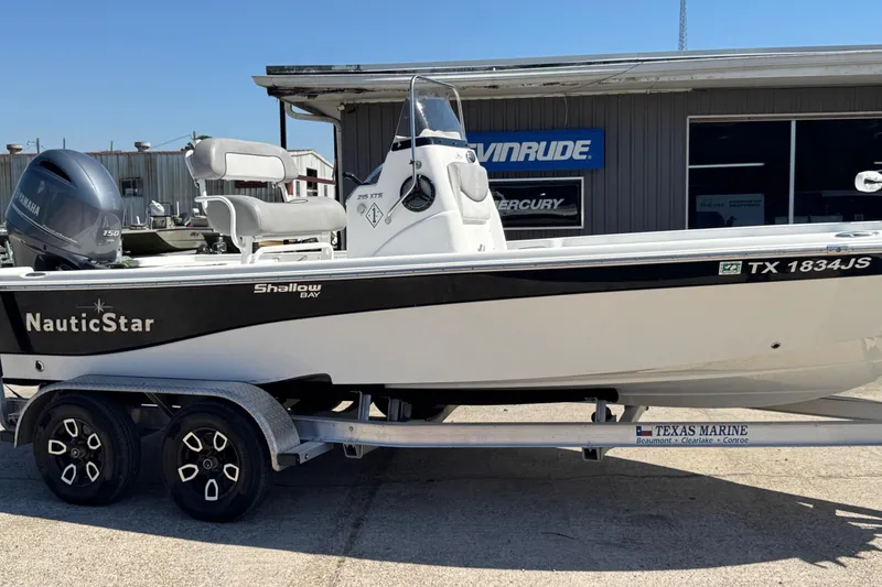 The Image of 2021 NauticStar 215 XTS Shallow Bay boat on trailer, parked outside marine shop. - 1