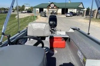 Slide: The Image of 2013 Crestliner Fisherman 145 CS boat interior with steering wheel and motor, parked near a building. - 5