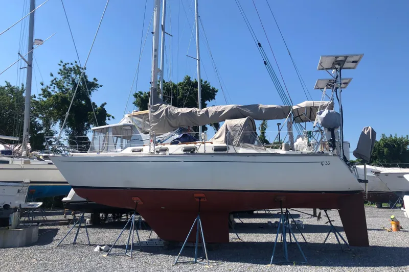 Slide: The Image of 1982 Tartan 33 sailboat on stands, covered, in a boatyard under clear blue sky. - 1