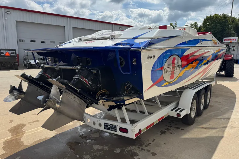 Slide: The Image of 2004 Cigarette 42 Tiger speedboat on trailer, vibrant graphics, dual propellers, parked outdoors. - 3