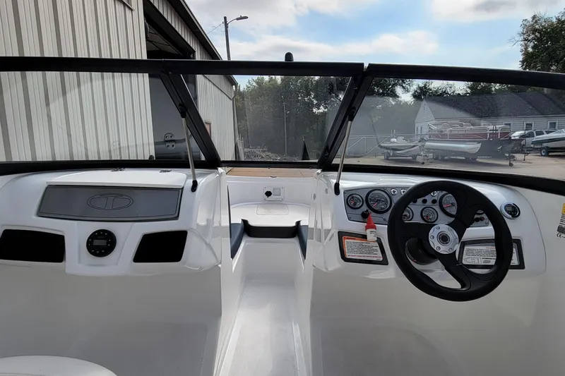 Slide: The Image of 2022 Tahoe 185 S WT boat dashboard with steering wheel and gauges, parked near a building. - 35
