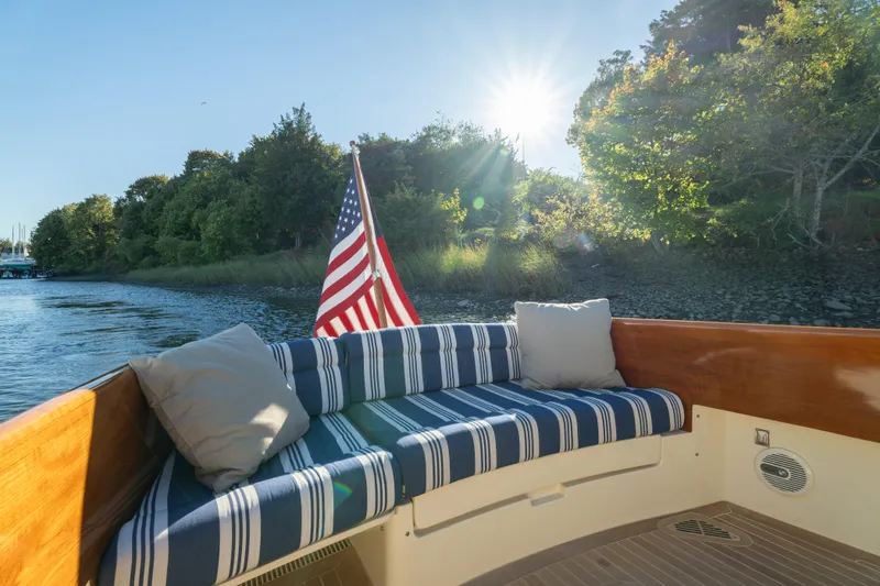 Slide: The Image of 2015 Hinckley Picnic Boat MK III with striped seating, American flag, and scenic water view. - 12