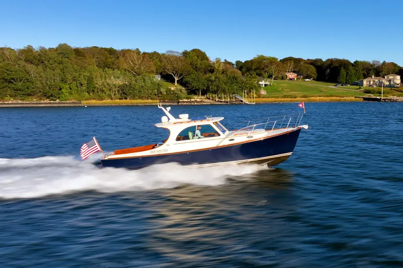 Slide: The Image of 2015 Hinckley Picnic Boat MK III cruising on a scenic lake with lush green shoreline. - 8