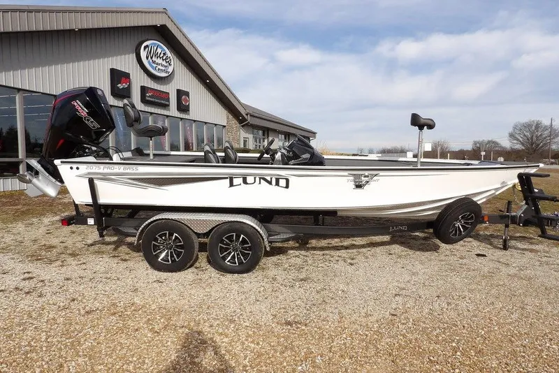 Slide: The Image of 2026 Lund 2075 Pro-V Bass XS boat on trailer outside marine center. - 3