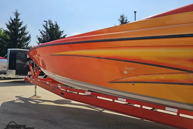 Slide: The Image of Orange 1995 Hustler 40 Fiore boat on trailer, parked outdoors under clear sky. - 8