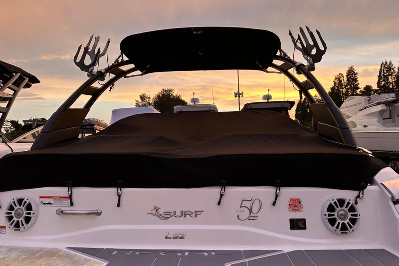 Slide: The Image of 2020 Regal LS2 Surf boat with cover at sunset, featuring sleek design and speakers. - 35