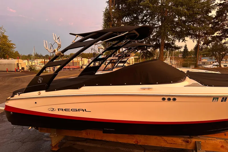 Slide: The Image of 2020 Regal LS2 Surf boat with black cover, parked outdoors near trees. - 36