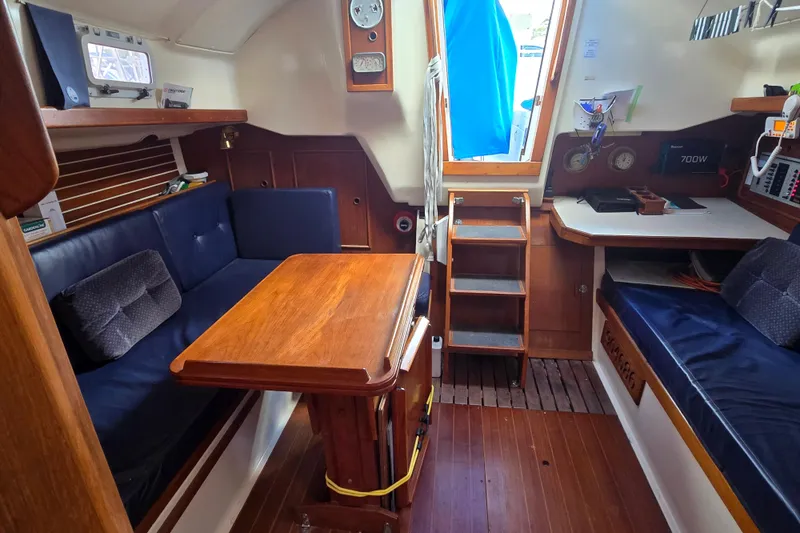 Slide: The Image of 1987 Nonsuch 30 Ultra yacht interior with wooden table, blue seating, and navigation equipment. - 20
