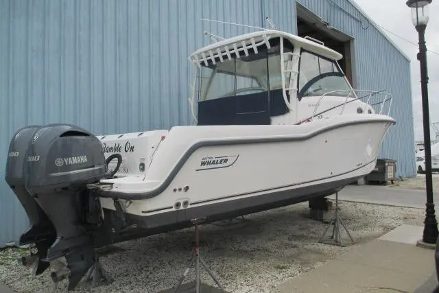 The Image of 2013 Boston Whaler 315 Conquest boat on stands near a blue building. - 0