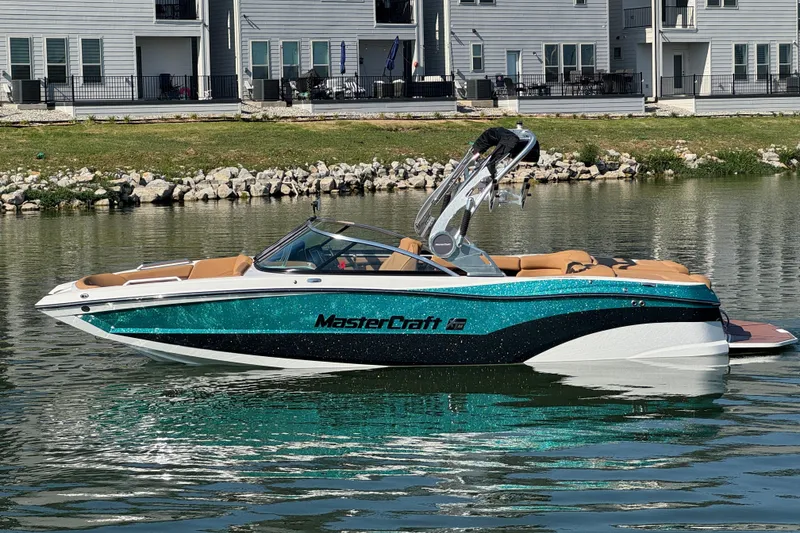 Slide: The Image of 2021 MasterCraft XT22 boat on a calm lake near modern homes. - 1