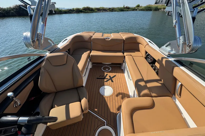 Slide: The Image of 2021 MasterCraft XT22 boat interior with tan seating and wood flooring on a sunny day. - 12