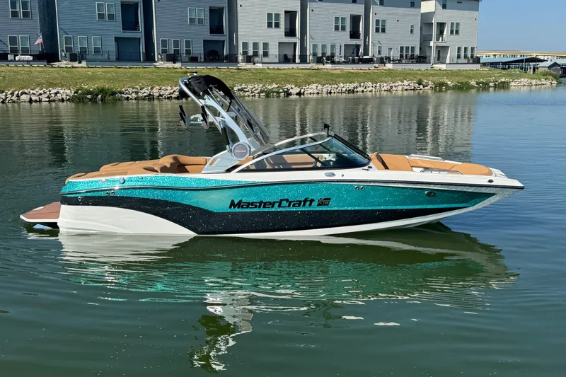 Slide: The Image of 2021 MasterCraft XT22 boat on calm water near modern buildings. - 2