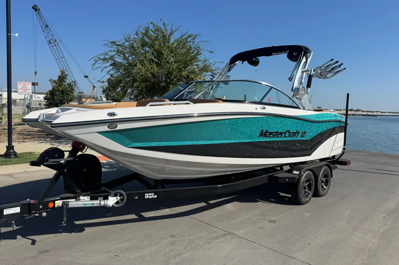 Slide: The Image of 2021 MasterCraft XT22 boat on trailer by waterfront, featuring teal and white design. - 6
